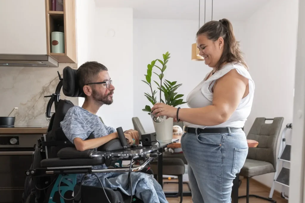 Support worker watering plant for disabled man